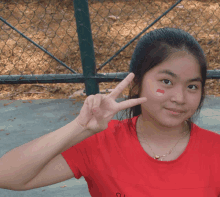 a girl with a red heart painted on her face is giving a peace sign