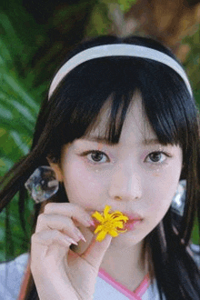 a young girl is holding a yellow flower in her hand in front of her mouth .