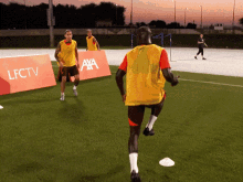 a man in a yellow vest is running on a soccer field in front of a sign that says lfc tv