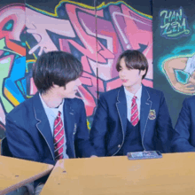 a group of young men in school uniforms are sitting at a table in front of a graffiti wall that says han