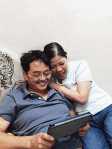 a man and a woman are sitting on a couch looking at a tablet