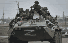 a group of soldiers riding on top of a military vehicle with the letter z painted on the side