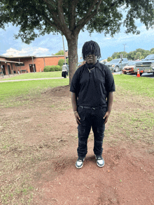 a man in a black shirt and black pants stands under a tree