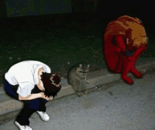 a man kneeling down next to a raccoon on the sidewalk