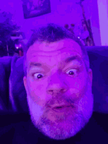 a man with a beard looks surprised in front of a purple light