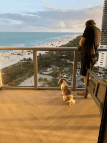 a man standing on a balcony with a dog looking out to the ocean