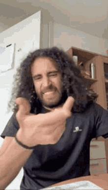 a man with long curly hair and a beard is making a funny face while sitting at a table .