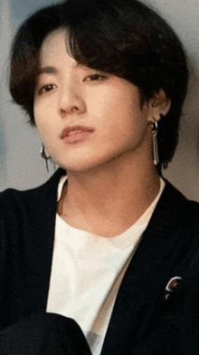 a close up of a young man wearing a black jacket and earrings