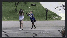 a boy is playing a trumpet while a girl stands behind him on a sidewalk .