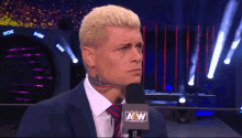 a man in a suit and tie is speaking into a microphone that says aew