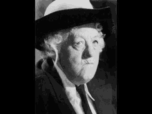 a black and white photo of an older woman wearing a cowboy hat and tie .