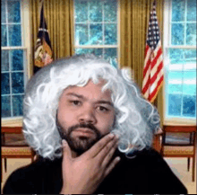 a man with a beard wearing a white wig is standing in front of a white house .