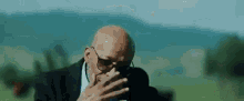 a bald man with glasses is smoking a cigarette in a field .