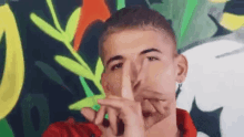 a young man in a red shirt is making a shhh gesture with his hands .