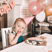 a little girl wearing a pink party hat is eating cake