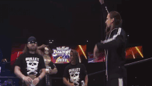 two men wearing black bullet club shirts stand in front of a screen