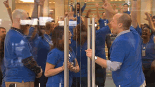 a group of people wearing blue shirts are standing in front of a glass door with their arms in the air