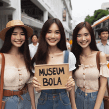 three women hold up a sign that says museum bola