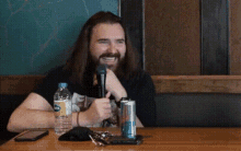 a man with long hair and a beard is sitting at a table with a bottle of aquafina water and a red bull can