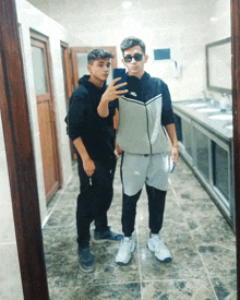 two boys are taking a selfie in a public restroom