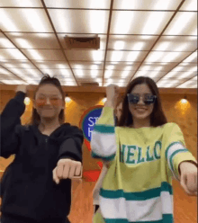 two girls are dancing together in a room while wearing sunglasses and sweaters .