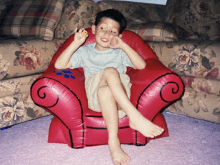 a young boy sits in a red chair with a paw print on the arm