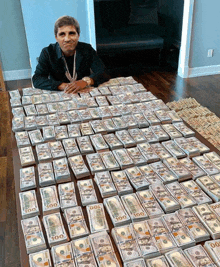 a man is sitting on a table with stacks of 100 dollar bills