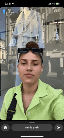 a woman in a green shirt is taking a selfie in front of a store window