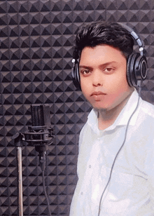 a young man wearing headphones and a white shirt is standing in front of a microphone