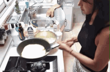 a woman in a black tank top is cooking on a stove in a kitchen with a carton of milk on the counter next to her