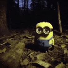 a yellow minion is standing in the woods at night .