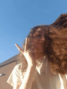 a woman with long curly hair is giving a peace sign