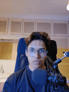 a young man wearing glasses is sitting in a chair with a microphone in front of him