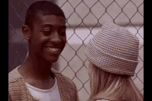 a man and a woman are standing next to each other in front of a chain link fence and smiling .