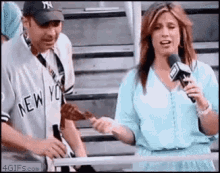 a man in a new york yankees jersey is standing next to a woman holding a microphone in a stadium .