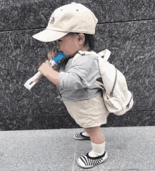 a little boy wearing a hat and a backpack is holding a stick