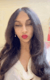 a woman wearing red lipstick and earrings looks at the camera with her eyes closed