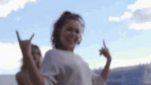 a woman is making a devil horns sign with her hands while dancing in front of a blue sky .