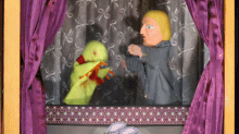 a purple curtain is behind a puppet holding a duck