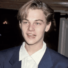 a young man wearing a blue jacket and white shirt is smiling