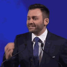 a man in a suit and tie is speaking into a microphone with the words un quebec qui rayonne partout dans le monde behind him