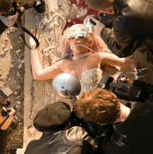 a woman with pearls around her neck is being photographed by a group of men