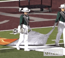 a man in a green and white uniform is holding a trumpet on a field with a giflab logo behind him