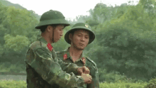 two soldiers are standing next to each other in a field . one of the soldiers is wearing a helmet .