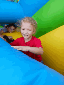 a little girl in a red shirt is playing in a bouncy house with other children