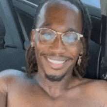 a shirtless man with dreadlocks and glasses is smiling while sitting in a car .