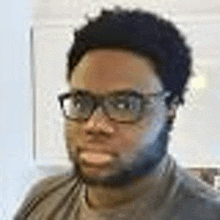 a man with glasses and a beard is standing in front of a white wall .