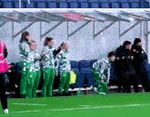 a group of people standing on a soccer field wearing green and white uniforms with the letter m on them