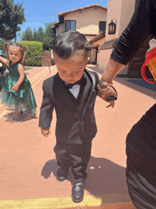 a little boy in a tuxedo is walking with a woman 's hand