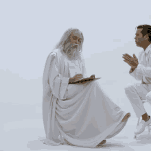 a man in a white robe is writing on a clipboard next to another man